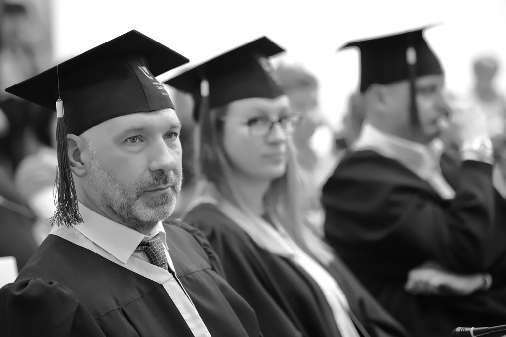 Zdjęcie z graduacji, trzech absolwentów na pierwszym planie, zdjęcie czarno-białe